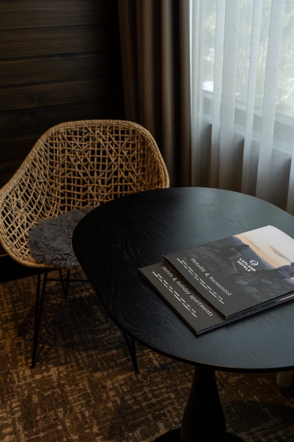A wicker looking chair with a table that is black and two information pamplets on it about the hotels activities and stuff