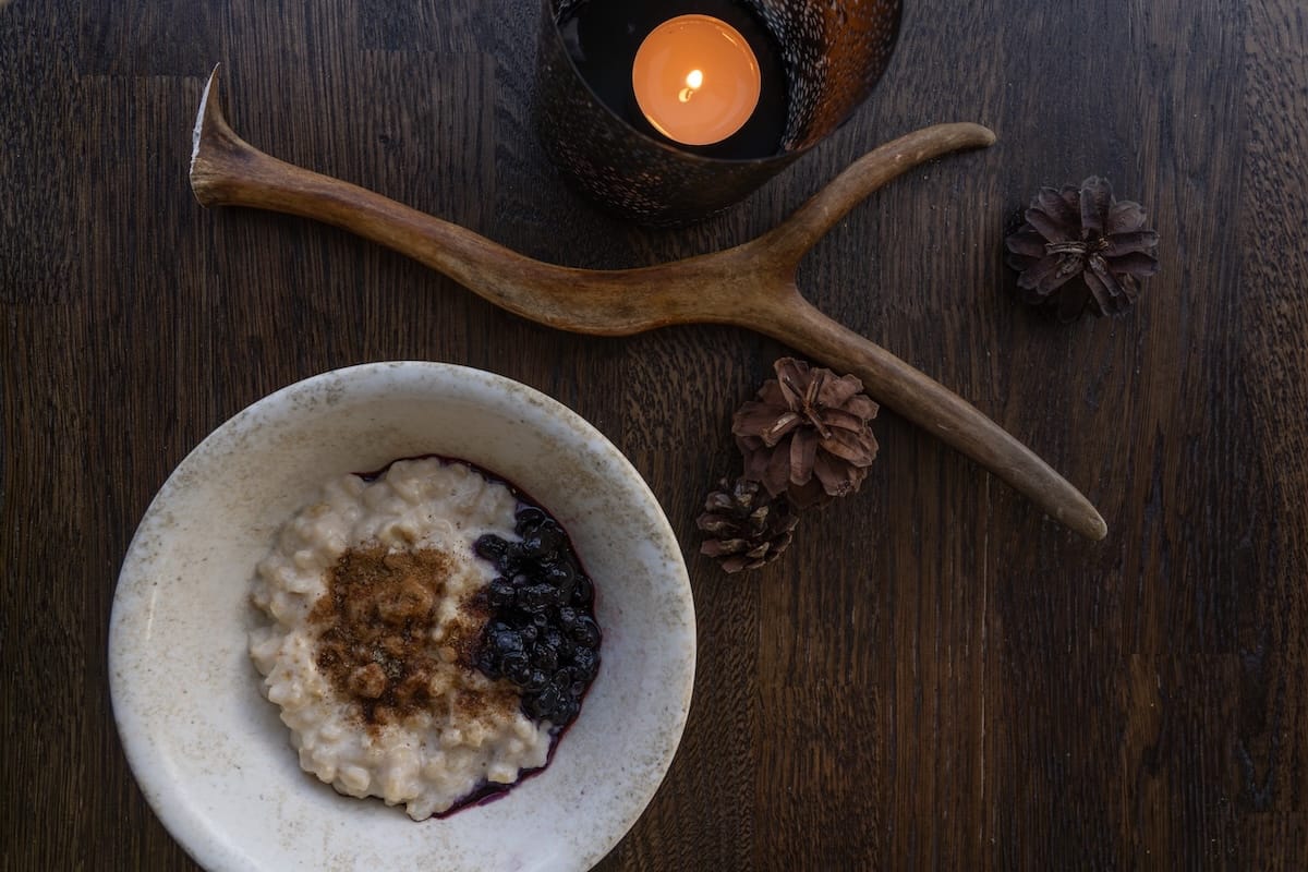 A porridge at Lapland Hotels with cinnamon, sugar, and blueberries topping it. There is a candle, pinecones, and a reindeer antler in the picture.