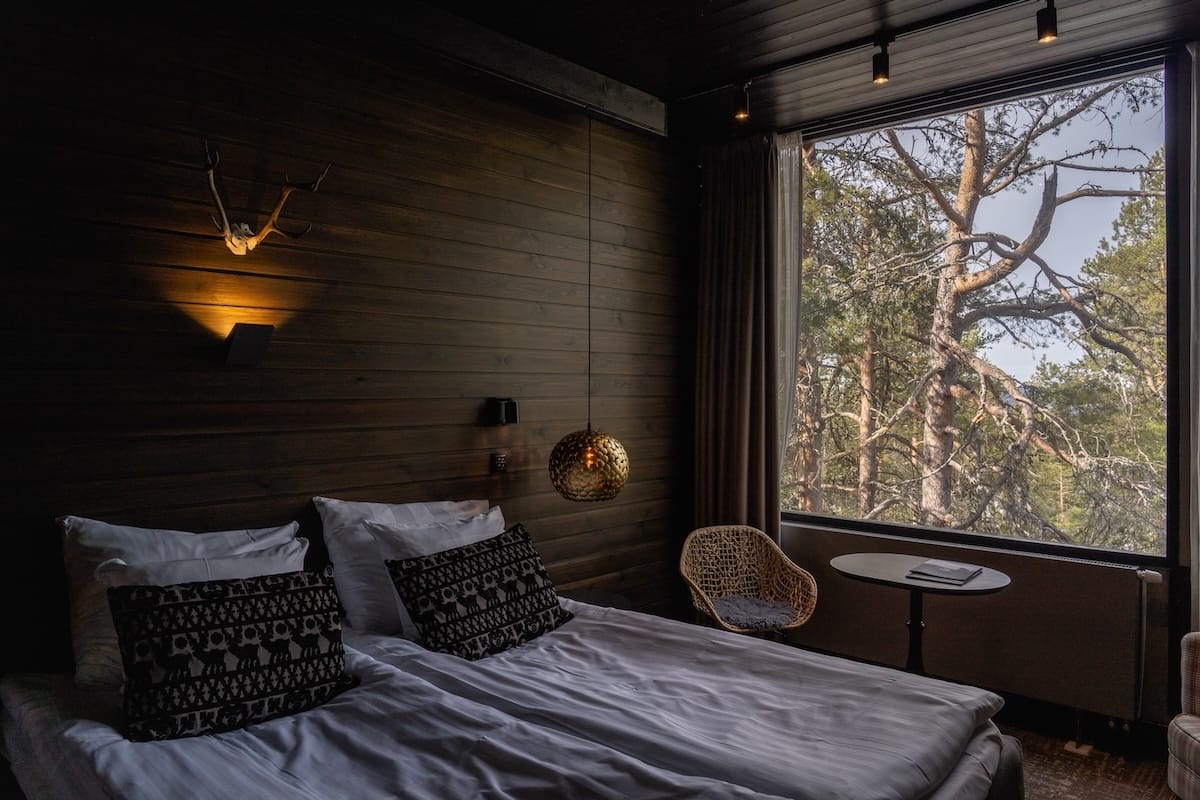 Lapland Hotels Sky Ounasvaara review - this is the view from my room with a lot of trees outside. There is a bed and pillows, as well as a chair and table in the background