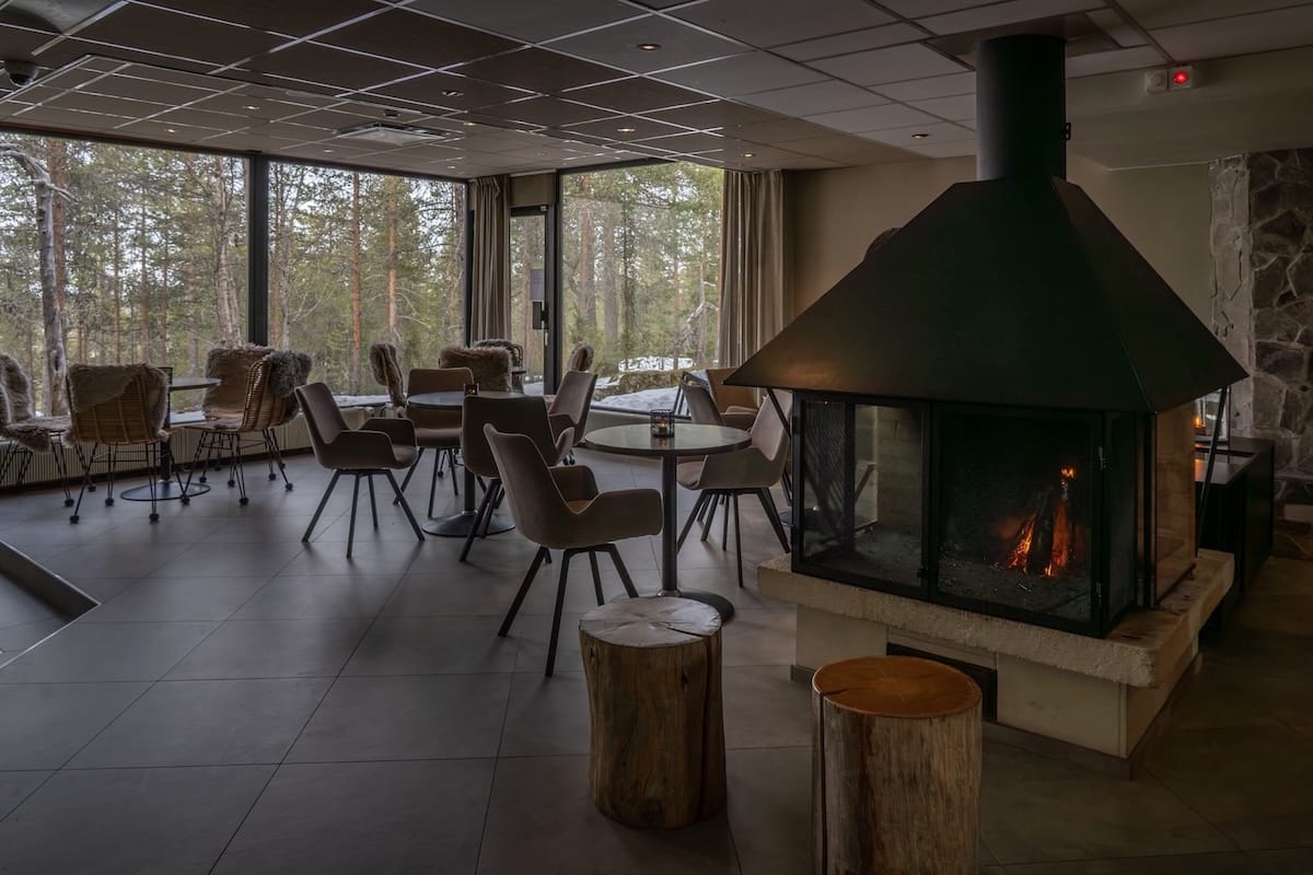 This is a fireplace with a seating area overlooking huge windows that show the forest